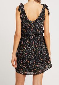 Robe noire à motifs floraux avec un dos en V profond, des bretelles à nouer et une coupe décontractée. Présente des motifs floraux colorés sur un tissu doux et léger.
