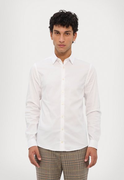 Chemise blanche à manches longues avec un col classique, fermeture à boutons à l'avant et tissu texturé. Assortie à un pantalon à carreaux aux tons neutres.