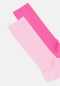 Bomullsockor i två nyanser: en helt ljusrosa och en ljusare rosa, med vertikal ribbad struktur och släta kanter.