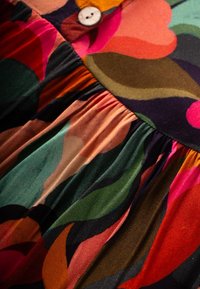 Farbenfrohes Kleid mit großen, abstrakten Blumenmustern in den Farben Pink, Grün und Orange. Verfügt über einen gerafften Rock und ein Knopfdetail.