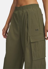 Olivově zelené cargo kalhoty z lehkého materiálu. Mají široký střih nohavic, elastický pas a velkou boční kapsu. Černý detail loga.
