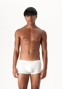 White cotton boxer briefs with a soft waistband, featuring a fitted design and minimal seams, worn by a model with a smooth torso against a plain background.