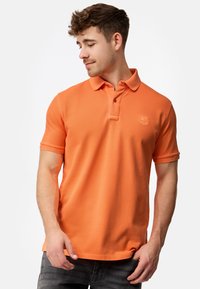 Oranje poloshirt met een klassieke kraag en een drie-knoopsluiting, met korte mouwen en een subtiele logo op de borst.
