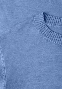 Gros plan sur un pull bleu clair, présentant un col côtelé, une texture lisse, et un design épuré sans motifs ni ornements.