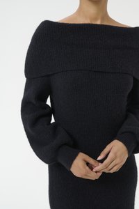 Maglione nero lavorato a maglia con design off-the-shoulder, tessuto texture e maniche lunghe e voluminose. Polsini e scollatura a costine lisce.