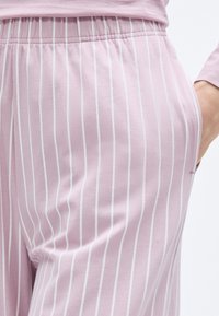 Tissu rose pâle avec des rayures verticales blanches, doté d'une ceinture élastique et de poches latérales. Texture douce et lisse, adaptée à une tenue décontractée.