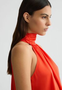 Rotes Haltertop mit gerafftem Halsdetail, aus glattem Stoff. Ärmelloses Design betont die Schultern und präsentiert eine fließende, entspannte Silhouette.