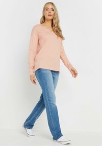 Helles rosa Langarmhemd mit V-Ausschnitt, kombiniert mit hellblauen geraden Jeans und weißen Sportschuhen. Glatte Textur, lässiges Design.