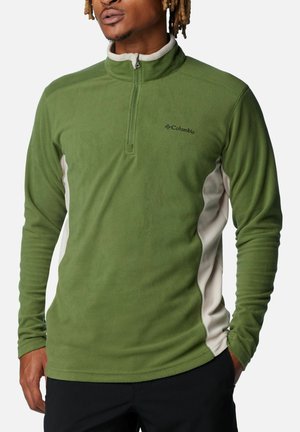 Pullover in pile verde con zip a quarto, pannelli laterali a contrasto color crema e logo Columbia sul lato sinistro del petto. Tessuto morbido, maniche lunghe.