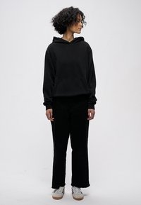 Mustast puuvillast kapuutsiga dressipluus esitasku ja nööriga kapuutsiga, mille juurde on kombineeritud mustad põlvikud ja valged tossud. Vabaaja ja mugav lõige.