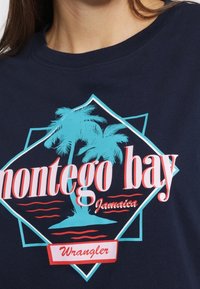 Námořnická modrá košile s tyrkysovými palmami a červeným textem "Montego Bay Jamaica" a logem značky "Wrangler".