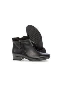 Botas de tobillo de cuero negro con un tacón bajo, cremallera lateral y suela de goma texturizada. Acabado liso con un collar de tela suave.