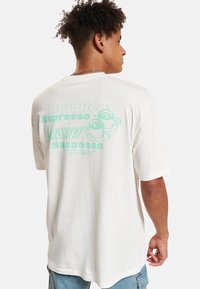 Weißes Baumwoll-T-Shirt mit kurzen Ärmeln, das auf der Rückseite hellblaue Schrift und Kaffeetassen-Grafiken zeigt. Lässige Passform mit rundem Ausschnitt.