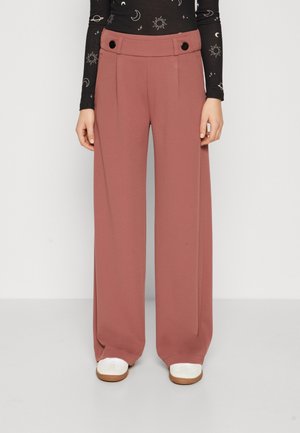 Pantalons larges couleur rose avec une texture lisse, dotés d'une taille haute, de plis et d'accents de boutons noirs à la taille.