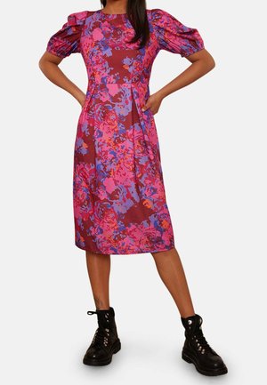 Femme portant une robe mi-longue à manches bouffantes avec un imprimé floral rose, violet et rouge, associée à des bottes de combat noires à lacets.