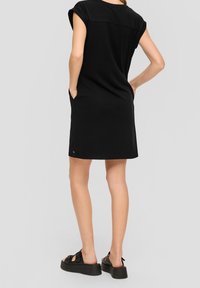 Musta, lyhythihainen mekko rentoa istuvuutta, sivutaskuja ja sileää pintaa. Yhdistetty paksujen mustien sandaalien kanssa. Yksinkertainen, polvipituinen muotoilu.