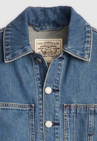 Veste en denim avec un lavage bleu, dotée d'un col chemise, de boutons sur le devant et d'une étiquette portant la mention "Levi Strauss & Co." Coutures visibles et poche.