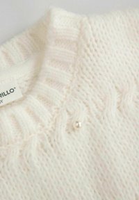 Kremowy sweter z dzianiny z prążkowanym dekoltem i teksturowanymi wzorami, ozdobiony małym perłowym guzikiem na przodzie.
