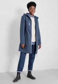 Granatowa wodoodporna kurtka z kapturem, z przodu na zamek i z bocznymi kieszeniami; noszona na lekkim swetrze i niebieskich dżinsach, w połączeniu z czarnymi botkami za kostkę.