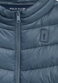 Vadderad blå väst med hög krage, dragkedja fram och märkespatch med en figur som håller en golfklubba. Slät, glänsande textur.