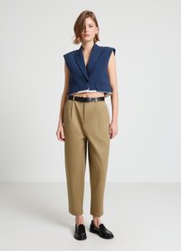 Marineblauer, kurz geschnittener Blazer mit Schulterpolstern, kombiniert mit hoch taillierter, hellbrauner Hose und einem schwarzen Gürtel; das Model trägt schwarze Loafers.