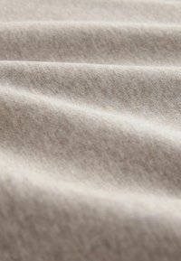 Lys beige stof med en blød tekstur, der har subtile diagonale linjer og bløde folder, hvilket skaber et draperet udseende.