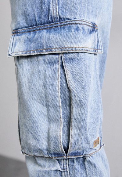 Lyseblå denim cargo bukser med afslappet pasform, synlige stikninger og en patchlomme på låret. Teksturen er blød og let slidt.