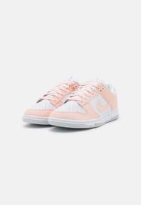 Nike sneakers with a white and soft pink leather upper, mesh tongue, perforated toe, and grey rubber sole. Solid laces and logo detail.