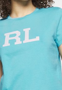 Osoba v světle modré košili s krátkým rukávem, na které jsou na hrudi vytištěna bílá písmena "RL".