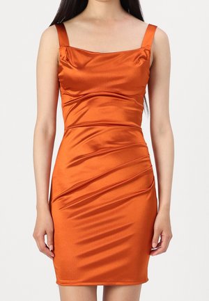 Kvinde iført en ærmeløs, tætsiddende, skinnende orange satin kjole med firkantet udskæring og opsamlet detalje på skørtet.