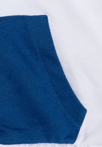 Medvilninė sportinė striukė su mėlyna kišene baltoje fone. Audinys turi lygų paviršių, o kišenė yra su rausvu raštu.