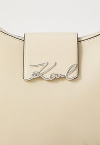 Sac à main en cuir beige avec un fermoir en métal argenté et des détails de couture. Texture lisse avec une forme arrondie et une fermeture éclair.
