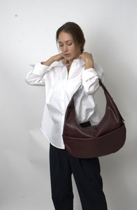 Brown leather shoulder bag with a soft, rounded shape and dual front pockets, worn by a person in a white shirt and striped pants.