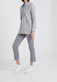 Grå stickad kavaj med slagkrage, en framficka, bärs över en blårandig skjorta och grå capribyxor, tillsammans med vita sneakers.