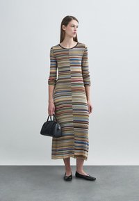 Ριγέ πλεκτό φόρεμα με μανίκια 3/4, με κάθετες ρίγες σε καφέ, μπλε και κόκκινο. Συνδυάζεται με μαύρη τσάντα χειρός και φλατ παπούτσια.