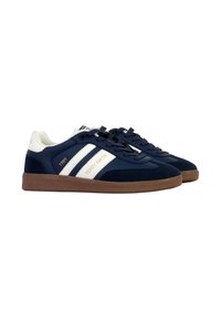 Zapatillas azul marino con rayas blancas, de material de ante y tela, suela de goma marrón, punta redonda, con el logo de "Teddy Smith" y el detalle de 1969.