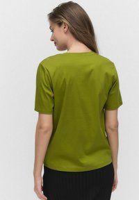 Olivgrön kortärmad t-shirt i mjuk bomull, med en rundad halsringning och avslappnad passform, sedd bakifrån.