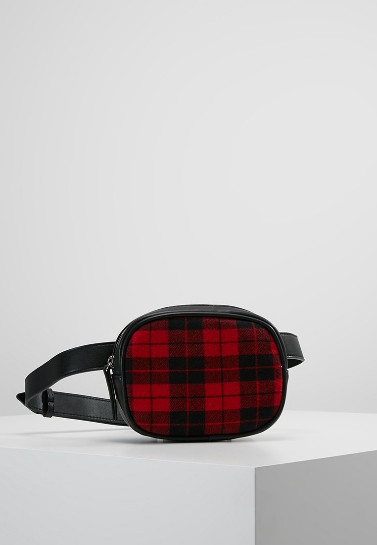 Sac en tissu écossais rouge et noir avec une forme rectangulaire arrondie et une bandoulière en cuir noir. Comprend une fermeture éclair et une texture lisse.