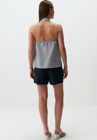 Top halter grigio con vestibilità morbida e texture semplice. Abbinato a pantaloni corti blu navy. Presenta una schiena aperta e piatta con cinghie annodate dietro il collo. Sandali bianchi.