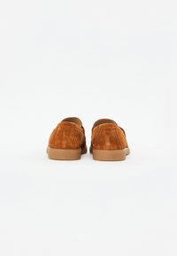 Braune Wildleder-Loafer mit weicher Textur, runder Form und flachen Gummisohlen. Rückansicht, die die Nähte und minimalistische Designdetails zeigt.