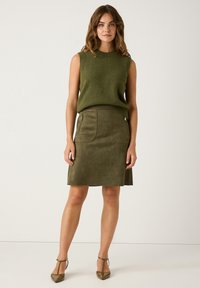 Olijfgroene mouwloze trui en bijpassende suede rok met zijzakken en een gladde textuur, gecombineerd met olijfgroene puntige hakken.