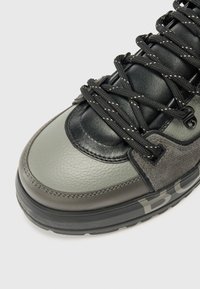 Detailní záběr na stylovou tenisku s kombinací šedých a černých materiálů, texturovanou kůží a výraznými tkaničkami pro bezpečné upevnění.