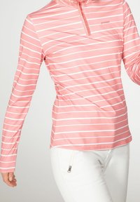 Růžová dlouhá mikina s bílými vodorovnými pruhy, s límcem na čtvrt zip a logem na levé straně. Měkká, elastická látka.