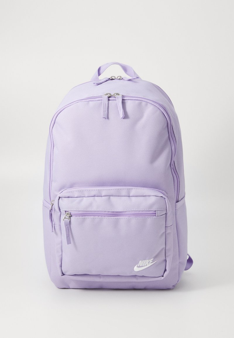 Violeta neilona mugursoma ar teksturētu virsmu, dubultām rāvējslēdzēm, priekšējo kabatu ar rāvējslēdzi un mazu baltu logotipu apakšējā priekšā.