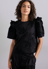 Top nero a maniche corte con ricami floreali testurizzati e paillettes, caratterizzato da maniche a sbuffo arricciate e scollatura rotonda.