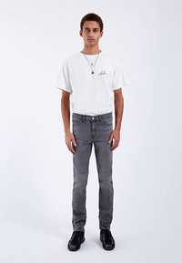 Jeans in denim grigio abbinati a una t-shirt bianca con scollo rotondo. I jeans hanno una vestibilità slim, mentre la t-shirt presenta un piccolo logo stampato.