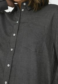 Dark gray linen shirt with buttoned collar, front pocket, and white buttons. The fabric features a subtle texture and relaxed fit.