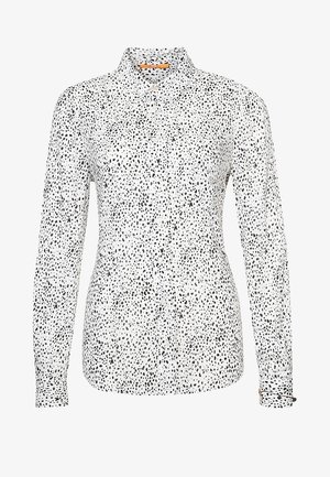 Wit overhemd met lange mouwen, knopen en een zwart patroon van onregelmatige stippen, voorzien van een klassieke kraag.