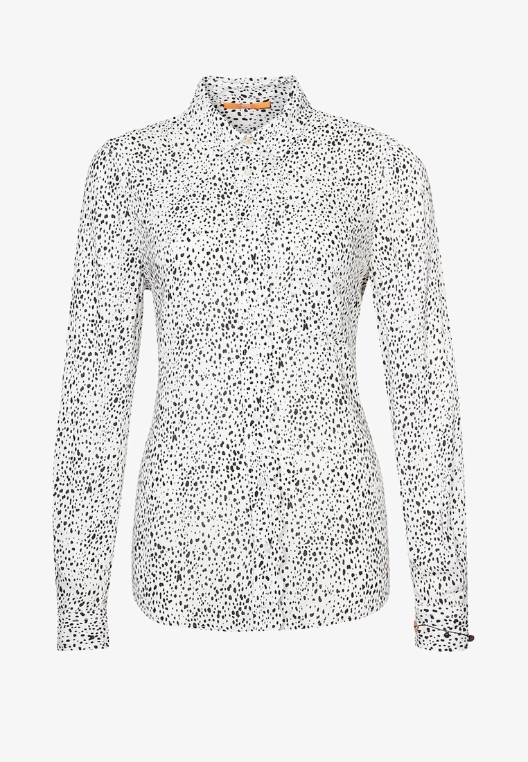 Chemise blanche à manches longues avec des boutons, ornée d'un motif de points noirs irréguliers et d'un col classique.