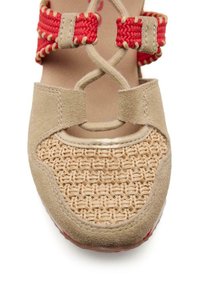 Ballet flat in suede beige con punta in paglia intrecciata, cinturini rossi intrecciati e dettagli metallici. Il design delle cinghie incrociate aggiunge un tocco di stile.